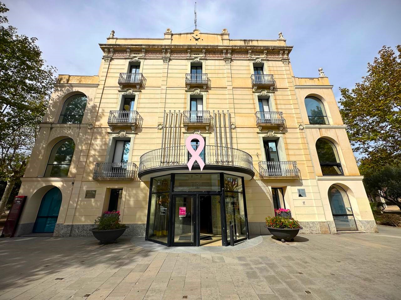 El llaç rosa penja del balcó de l'Ajuntament en commemoració al Dia Mundial contra el Càncer de Mama 2023.