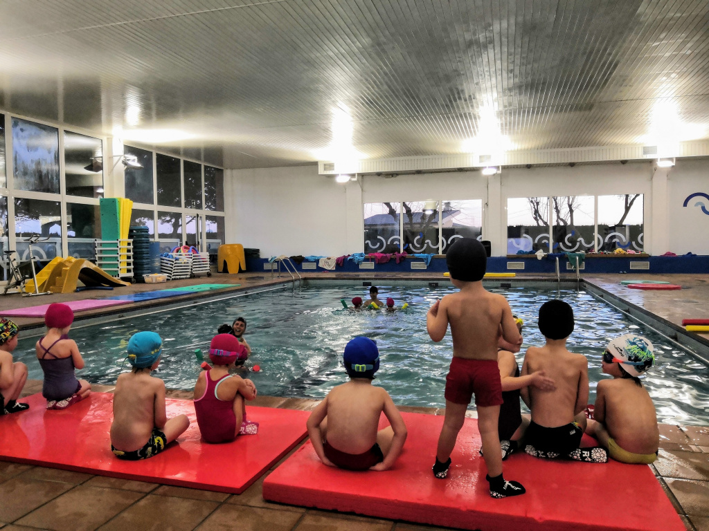 Nens i nenes a la piscina coberta esperant indicacions del monitor que està a l'aigua